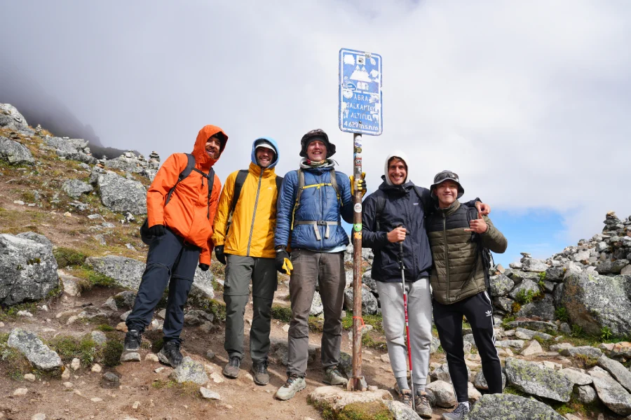 Group of trekkers standing at snowy Abra Salkantay with a trail sign and snow-capped peaks | Conde Travel Adventures