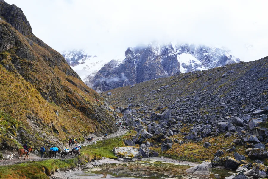 Group of hikers ascending a rugged mountain path on the Salkantay Trail with snowy peaks in the background | Conde Travel Adventures