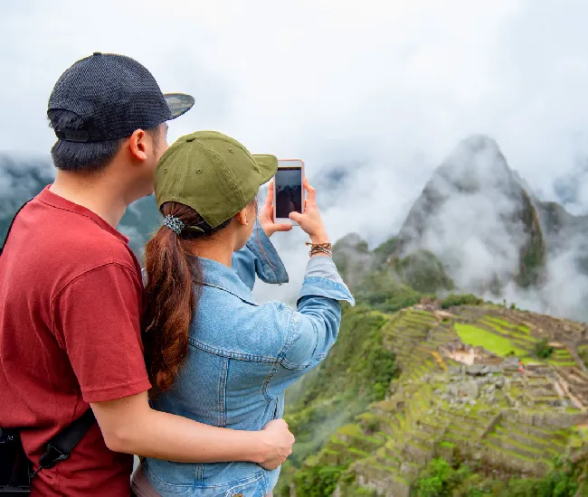 Two tourists taking a photo of Machu Picchu from a foggy viewpoint during an overnight visit | Conde Travel Adventures