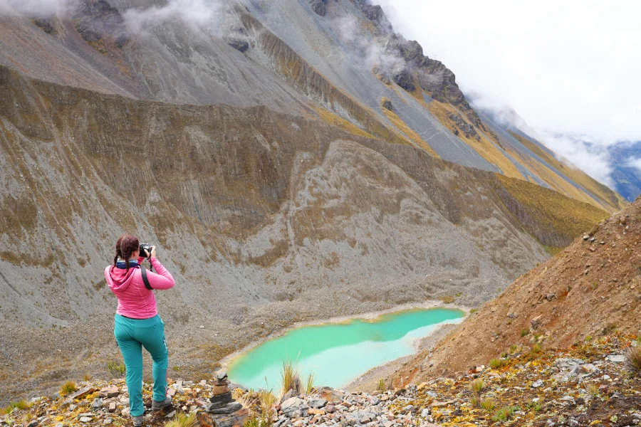 Female traveler taking a scenic photo of Incachiriasqa Lake surrounded by mountain peaks | Conde Travel Adventures