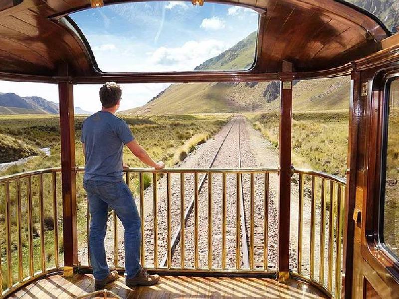 Male traveler enjoying panoramic views from the rear balcony of the Andean Explorer train on its route through the Peruvian highlands between Cusco and Puno | Conde Travel Adventures
