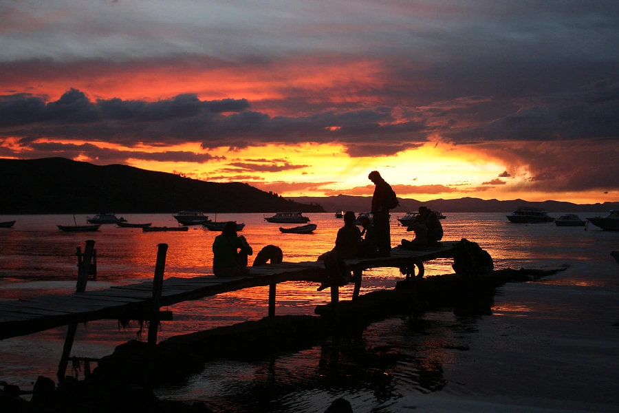 Silhouettes of people on a dock at sunset over Lake Titicaca, with boats floating near Puno, Peru | Conde Travel Adventures