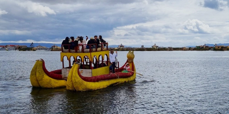 Group of tourists on a colorful double-decker totora reed boat paddling through the calm waters of Lake Titicaca near the Uros floating islands in Puno, Peru | Conde Travel Adventures