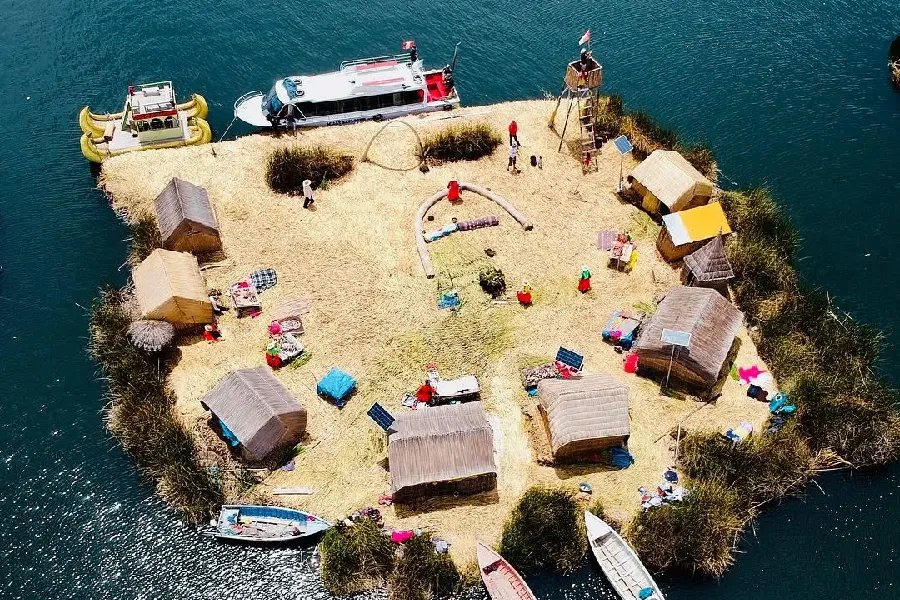 Aerial photo of a traditional Uros floating island with totora houses and tourist boats on Lake Titicaca, southern Peru | Conde Travel Adventures