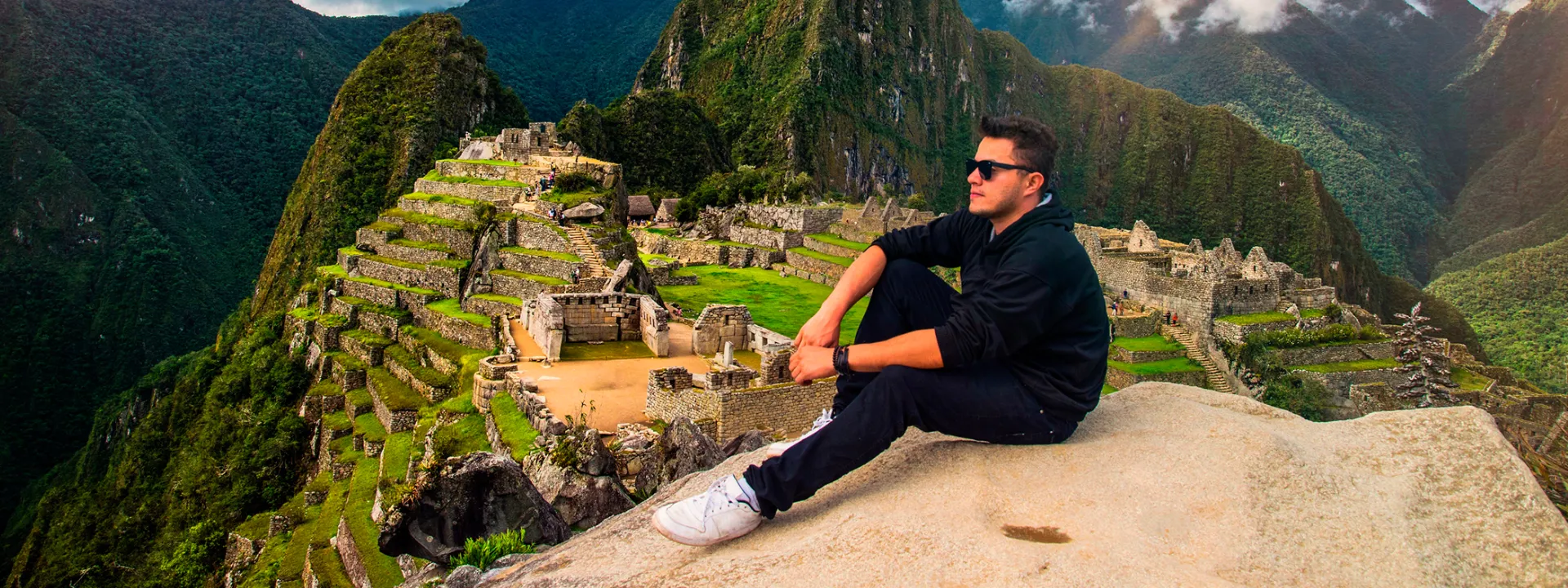 Traveler sitting on a rock overlooking Machu Picchu ruins during a private tour experience in the Andes mountains.