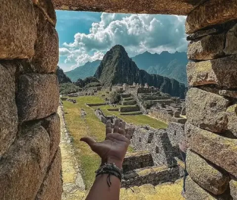 Hand pointing at Machu Picchu ruins framed by stone walls | Conde Travel Adventures